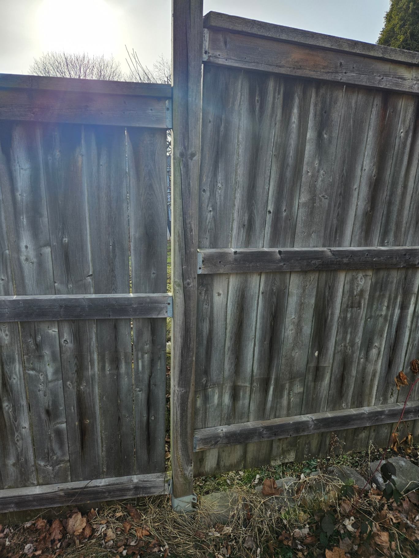 A galvanized steel channel stake fastened alongside a warped fence post — the panels now hang off thin sheet metal that flexes with every gust — Cambridge, Ontario, May 2026.