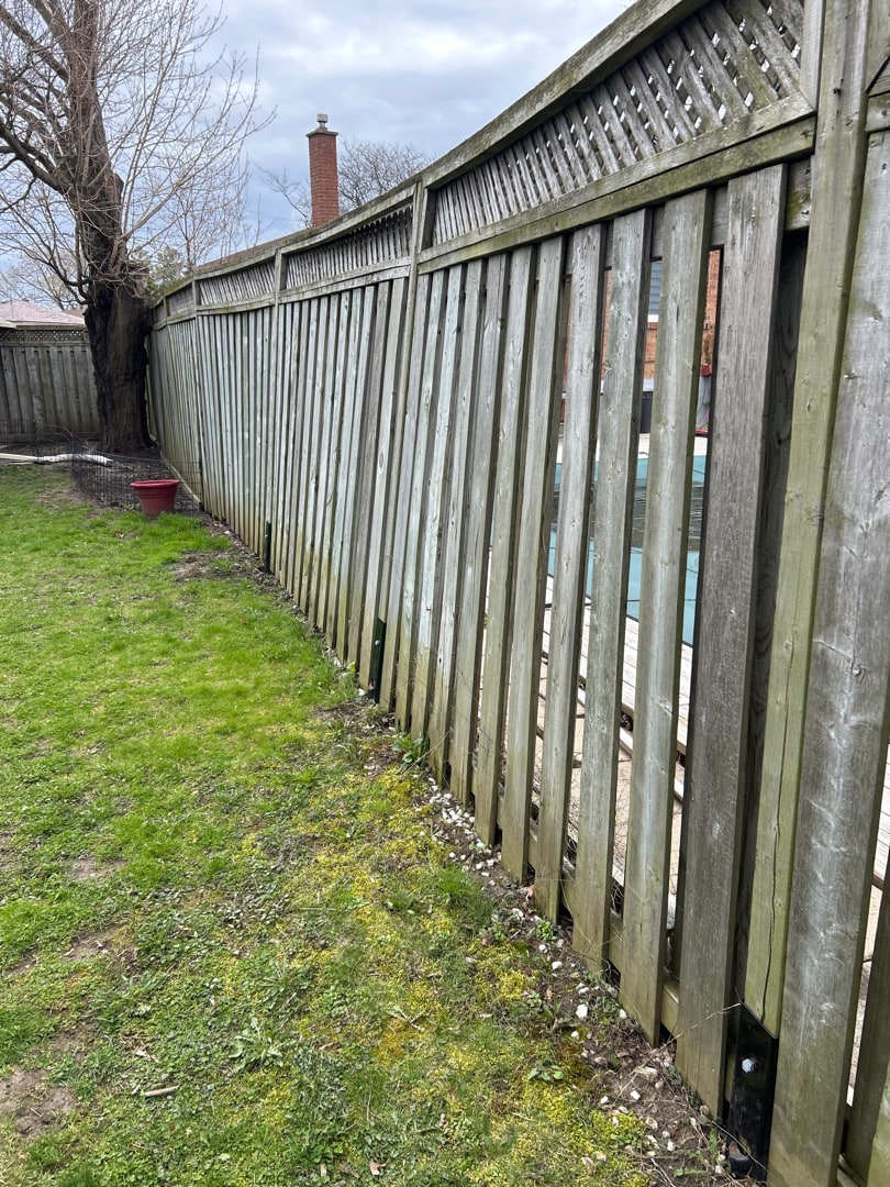 An entire lattice-top fence run leaning toward a pool deck with black E-Z Menders visible at the post bases — the plates went along for the ride — Scarborough, Ontario, April 2024.