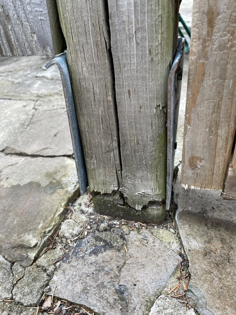 The clearest picture of why sockets fail: this spiked post base's side flanges have splayed wide open while the shrunken, rotted post crumbles inside them — nothing is gripping anything — Cambridge, Ontario, April 2024.