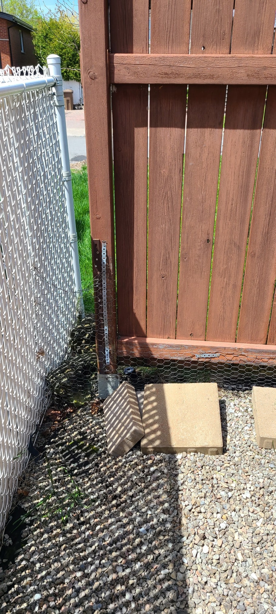 Two layers of hardware-store fix on one post: a spiked post base at grade with a perforated steel strap screwed up the post above it — neither layer stopped the lean — Laval, Quebec, May 2024.